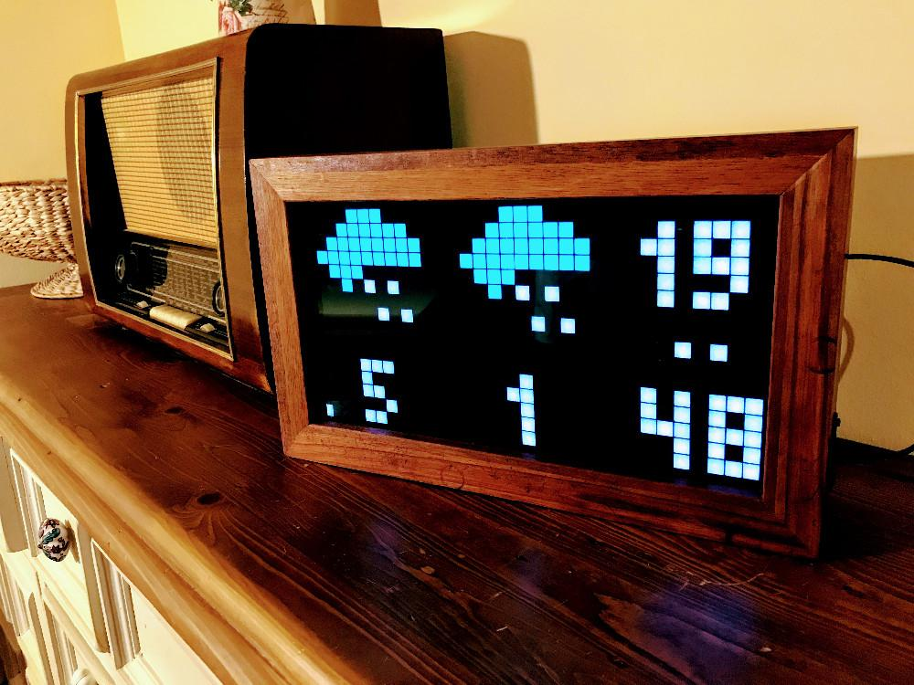 Framed LED matrix display showing weather icons and temperature on a shelf