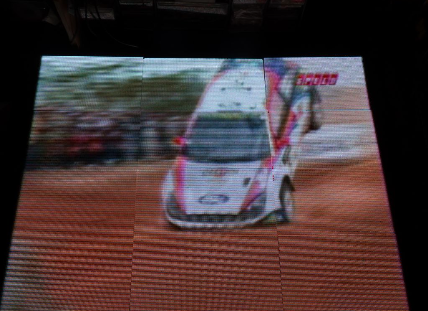 Large tiled LED matrix wall displaying a racing car video scene